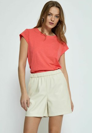 Camisa de manga corta color coral combinada con shorts de cuero sintético color crema. La camisa tiene un corte holgado y una textura suave.