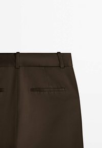 Pantalon sur mesure marron foncé montrant la partie supérieure arrière avec passants de ceinture et deux poches passepoilées horizontales.