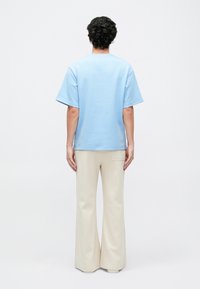 Camiseta de algodão azul claro com mangas curtas, corte solto, decote redondo, combinada com calças largas em creme com um bolso traseiro.