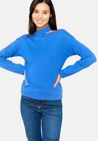 Pull en tricot bleu avec un col montant, des manches longues et une coupe décontractée, associé à un jean en denim. Texture douce et couleur vive.
