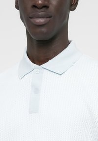 Polo bleu clair en maille avec un petit col, deux boutons et un tissu texturé. Vue en gros plan mettant en valeur les détails des coutures.