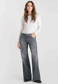 Jean flare en denim gris délavé, doté d'une taille mi-haute, d'un design à cinq poches et de coutures décoratives le long des coutures.