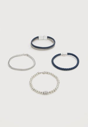 Quattro braccialetti esposti su una superficie chiara: due in pelle intrecciata blu navy con chiusure, uno in catena d'argento e uno in argento con perline e chiusura decorativa.