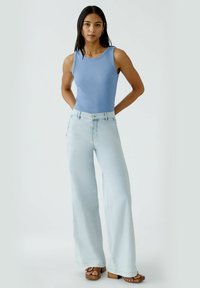 Light blue ribbed tank top paired with light wash wide-leg jeans; earthy brown platform heels with decorative accents. Simple, casual outfit.