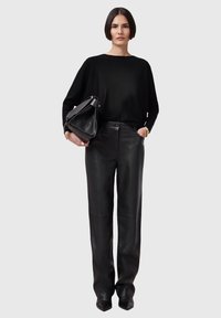 Black knit sweater paired with high-waisted black leather pants. The model holds a structured, black leather handbag. Smooth textures.