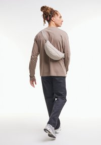 Grå vadderad axelväska bärs över en lös beige långärmad skjorta och mörka byxor, skor med grå och svarta detaljer.