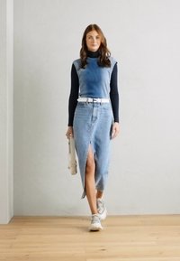 Blå ribbad croptop över en svart turtleneck, ihop med en högslitsad denimkjol och vit bälte, kompletterad med ljusa sneakers och en handväska.