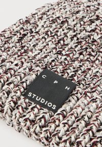 Căciulă tricotată din fire multicolore în nuanțe de gri, negru și burgund. Are o etichetă din material textil negru cu inscripția „CPH STUDIOS” în text alb.