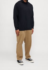 Pull à col roulé bleu marine, en coton, coupe ample, associé à un pantalon beige et des baskets basses noires avec semelles et lacets blancs.