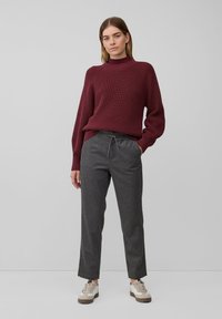 Burgunderfarbenes, geripptes Strickpullover kombiniert mit grauen, lässigen Hosen. Die Sneakers sind cremefarben mit braunen Akzenten. Minimalistisches Design und neutrale Farben.
