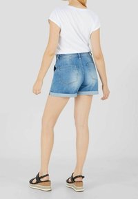 Vaaleat denim-shortsit, joissa on kääritty helma ja kaksi takataskua, yhdistetty valkoiseen lyhythihaiseen t-paitaan ja mustiin korkokenkiin.