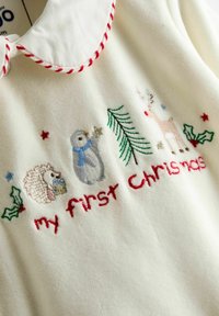 Vêtement en polaire blanc comportant des animaux brodés : un hérisson, un pingouin avec une écharpe bleue et un renne, avec le texte "mon premier Noël" en rouge.