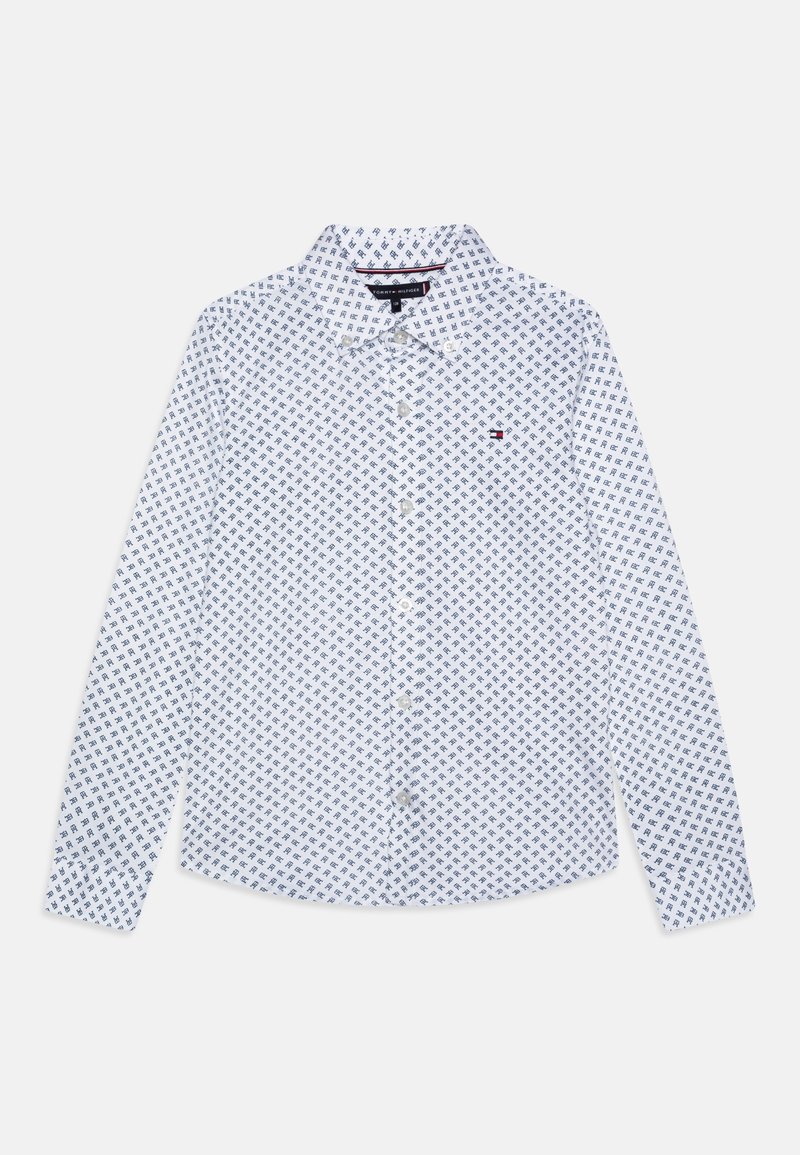Chemise blanche à manches longues avec un petit motif géométrique bleu marine répétitif et un petit logo rouge, blanc et bleu sur la poitrine.