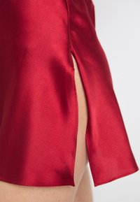 Rotes Satin-Kleid mit einem seitlichen Schlitz, glatter Textur und einer fließenden Silhouette. Der Saum ist scharf mit ordentlichen Nähten entlang der Kante.