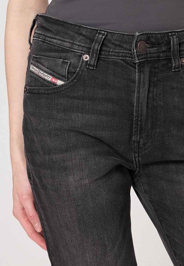 Czarne dżinsy o dopasowanym kroju, z widoczną metką na przedniej kieszeni i detalami z metalu, prezentujące lekko przetartą teksturę.