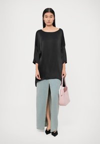 Melnas satīna blouse ar plašiem piedurkņiem, apvienota ar gaiši zilu maksi džinsu svārku ar priekšējo šķēlumu. Tur rokās gaiši rozā rokassomu. Melni zābaki.
