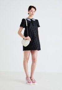Black dress with short puff sleeves and a decorative white floral collar. Paired with a cream heart-shaped bag and pink platform shoes.