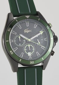 Montre chronographe noire et verte avec un cadran gris texturé, des accents verts, de grands marqueurs d'heure et un bracelet en caoutchouc avec texture nervurée.