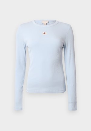 Šviesiai mėlynas ilgomis rankovėmis marškinėlis iš gofruotos medžiagos. Turi apvalų kaklo iškirpimą ir mažą raudoną CK logotipą krūtinėje.