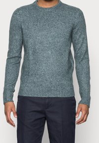 Teal stickad tröja med rund hals, ribbade ärmslut och nederkant. Tillverkad av mjukt, texturerat tyg, den har en figurnära silhuett.