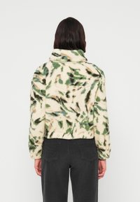 Chaqueta corta y acolchada en color crema con un patrón de hojas verdes y marrones. Cuenta con un cuello alto y tela texturizada.