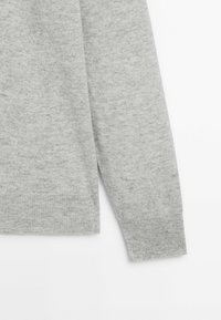 Harmaa pitkähihainen neulepaita, joka on valmistettu pehmeästä neuloksesta. Siinä on ribbireunat ja -hihansuut sekä hieman teksturoitu pinta.