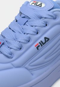 Κοντινό πλάνο ανοιχτού μπλε αθλητικού παπουτσιού FILA που δείχνει υφασμένα κορδόνια, ραμμένες λεπτομέρειες και το λογότυπο FILA σε μαύρο και κόκκινο στην πλευρά και στη γλώσσα του παπουτσιού.