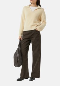 Jasnobeżowy dziany sweter z dekoltem w serek i dużym kołnierzem, zestawiony z ciemnobrązowymi spodniami o szerokich nogawkach oraz teksturowaną ciemną torbą.