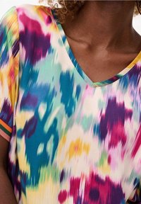 Top a maniche corte, con scollo a V, caratterizzato da un vivace motivo tie-dye in tonalità di blu, viola, giallo e rosa. Tessuto morbido e leggero.
