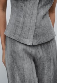 Szary lniany dwuelementowy zestaw składający się z dopasowanej bluzki z szerokim dekoltem oraz teksturowanych, lekko luźnych spodni z subtelnymi pionowymi liniami.