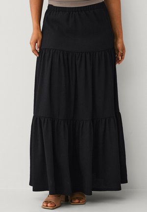 Black tiered maxi skirt with elastic waistband worn with tan open-toe block heel sandals, standing against a plain light background.