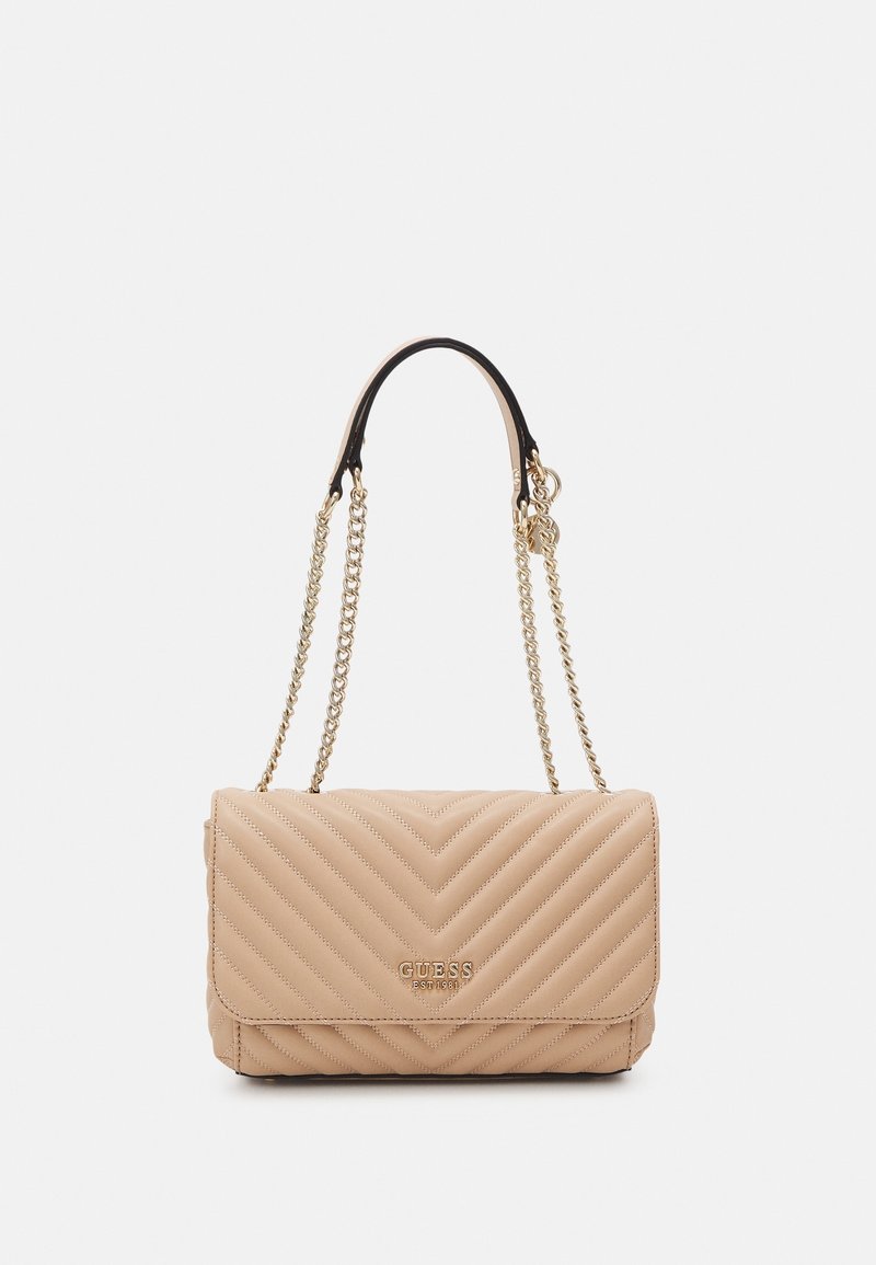 Sac à main matelassé beige avec des bandoulières en chaîne dorée et le logo « GUESS EST 1981 » sur le rabat avant, sur un fond uni.