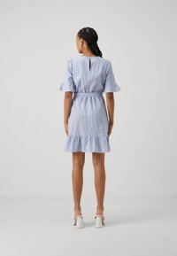 Randig blå klänning med utsvängda ärmar, smal midja och volangnederdel. Ryggen har en nyckelhålöppning. Modellen bär vita klacktofflor.