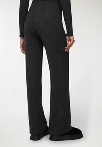 Ciemnoszare, prążkowane spodnie w stylu dzwonów z teksturowanej tkaniny. Cechują się wysokim stanem i gładkim wykończeniem na dole. Widoczne czarne obuwie.