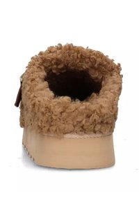 Zapato marrón de tipo mocasín, con un revestimiento de lana rizada y texturizada, y una suela de madera clara maciza con un leve tacón.