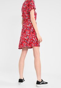 Czerwona sukienka w kwiaty z krótkimi rękawami, dopasowana w talii, z rozszerzonym dołem. Nosić z czarnymi sneakersami z białymi podeszwami i sznurówkami.