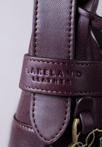 Dark burgundy leather strap with embossed text "LAKELAND LEATHER," sturdy stitching, and a metal clasp featuring an intricate design.
