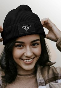 Black knitted beanie with a folded brim featuring a rectangular label that says "valhalla" and an illustration of crossed axes.