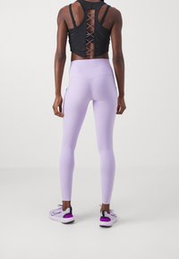 Zwarte crop top met een crisscross rugontwerp, gecombineerd met lichtpaarse leggings en sport schoenen met paarse accenten. Glad, aansluitend textuur.
