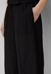 Zwarte, gestructureerde broek met een gekreukte stofafwerking, voorzien van een elastische tailleband met trekkoord en zijzakken voor functionaliteit.