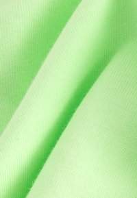 Lichtgroene stof met een gladde textuur, voorzien van een fijn breipatroon en enige rek, gerangschikt in zachte, vloeiende plooien.
