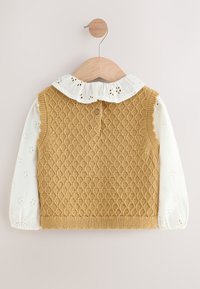 Veste tricotée jaune moutarde avec motif en losanges texturé, superposée à un chemisier blanc doté d'un col à volants et de détails floraux en découpe ajourée.