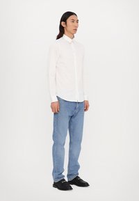 White long-sleeve button-up shirt, light blue denim jeans, and black shoes, worn by a standing figure against a plain white background.