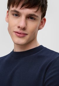 Granatowy sweter z okrągłym dekoltem, prążkowanymi mankietami i gładką teksturą, noszony przez modelkę z krótkimi włosami i kolczykiem, na neutralnym tle.