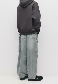 Sweat à capuche gris oversize avec poche kangourou avant, associé à un pantalon cargo gris clair à taille haute et coupe ample, doté de poches latérales.