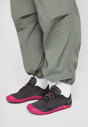 Zapatillas Merrell ligeras en negro y rosa, usadas con calcetines blancos y pantalones verde oliva con puños elásticos.