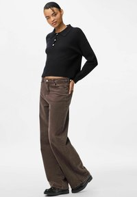 Crni pleteni džemper s ovratnikom i tri gumba, uparen s smeđim hlačama širokih nogavica i crnim cipelama, prikazan na neutralnoj podlozi.