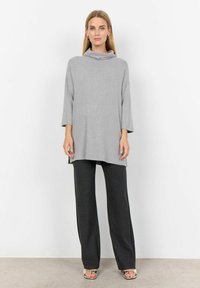Light gray oversized top with a cowl neck and three-quarter sleeves, paired with dark gray pinstriped trousers and metallic heeled sandals.