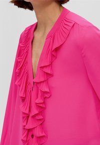 Närbild av ett nackeområde med en livfull rosa blus med djup ringning och dekorerande volangkant längs framsidan.