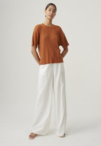 Rust-colored ribbed short-sleeve top paired with white wide-leg pants. Simple design with a relaxed fit. Smooth texture, discreet detailing.